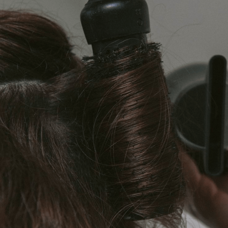 Person using a hair dryer on their hair with a blurred background