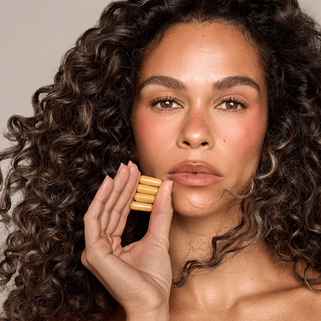 Woman holding a gold bar against her cheek with a neutral background