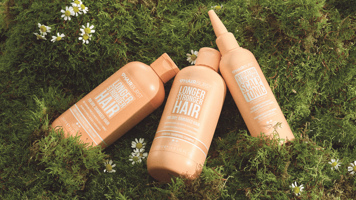 Three bottles of hair care products on a grassy background with flowers.